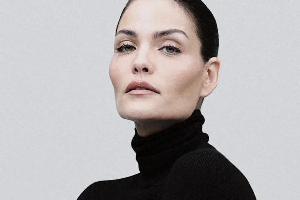 Imagem colorida mostra rosto anguloso de mulher branca com olhos verdes. Ela tem os cabelos presos e veste blusa de gola alta preta - Metrópoles