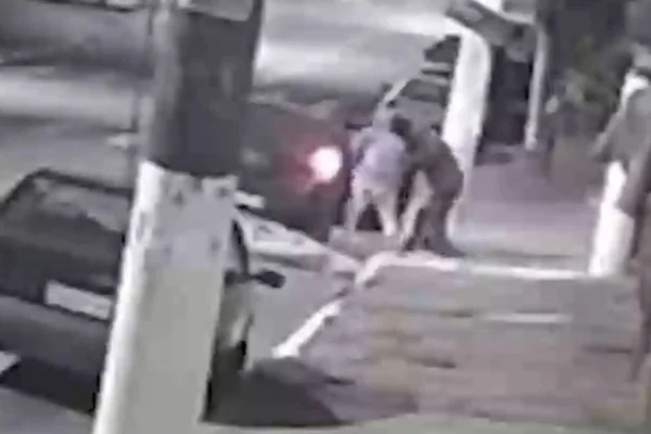 Imagem em preto e branco de dois homens ao lado de um veículo. Metrópoles