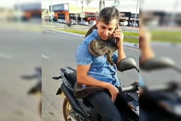 Foto colorida de homem com jiboia enrolada no pescoço - Metrópoles