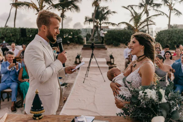 homem e mulher de branco um de frente para o outro. no colo da mulher um bebê sendo amamentado