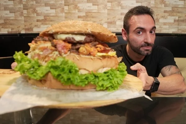 Foto colorida de um homem segurando uma comida gigante - Metrópoles