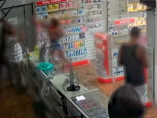 Imagem colorida de quatro pessoas dentro de uma farmácia brigando entre si. Uma delas está com uma cadeira erguida