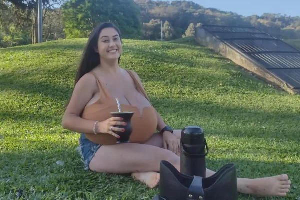 Foto colorida de mulher sentada em grama tomando chimarrão - Metrópoles