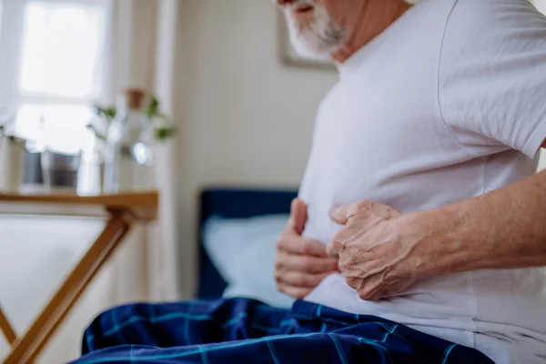 Foto colorida de homem mais velho com as mão na barriga, como se estivesse sentindo dor - Metrópoles.