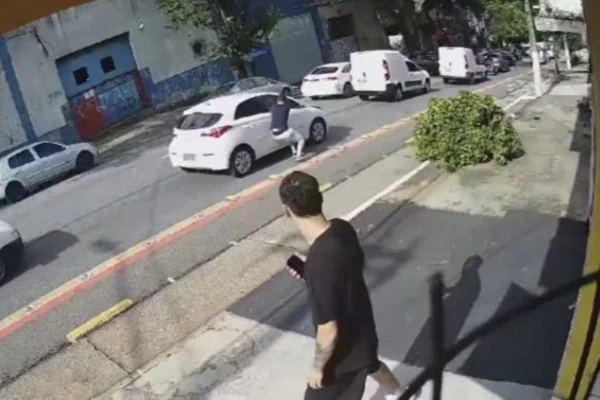 Imagem colorida mostra bandido quebrando vidro de carro com o cotovelo para roubar celular do motorista em São Paulo; eles agiam em dupla - Metrópoles