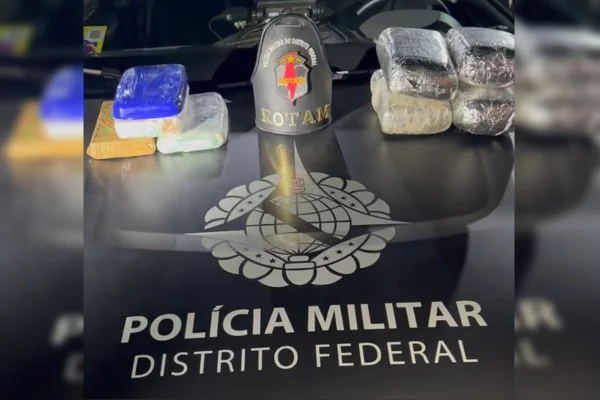 Imagem colorida de oito tabletes de drogas sobre uma viatura preta da PMDF