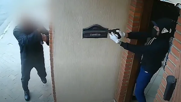 Um homem de capuz e máscara aponta arma para homem vestido de preto - Metrópoles