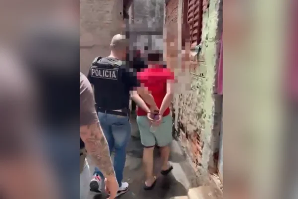 Imagem colorida de homem de camisa vermelha preso. Metrópoles