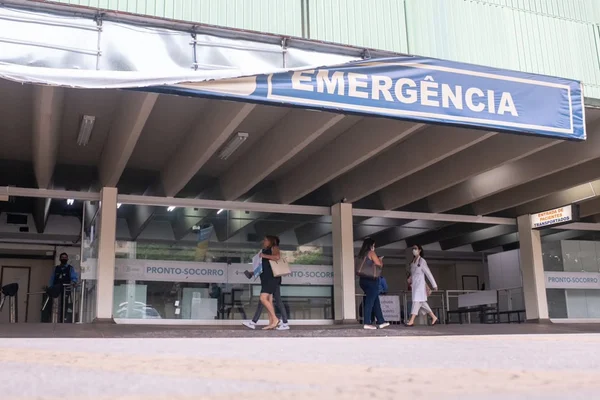 Fachada do Hospital de Base do Distrito Federal, com banner escrito "Emergência" caindo pela metade