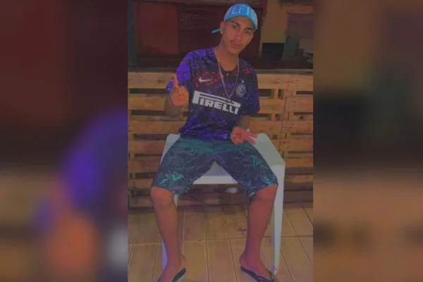Foto de um homem com camisa roxa e boné sentado em uma cadeira