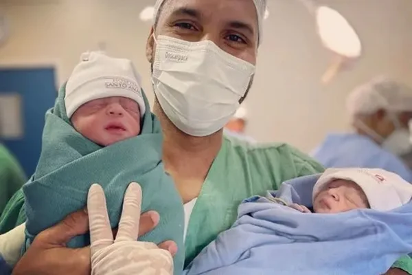 Foto colorida de um homem branco que conquistou o direito de pai solo e segurando as suas duas filhas gêmeas - Metrópoles