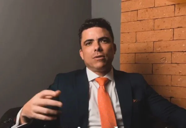 Homem branco com olhos olhos azuis, vestido com paletó preto e gravata laranja - Metrópoles