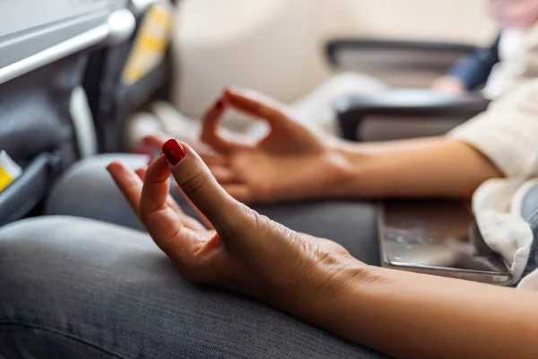 Imagem que foca nas mãos de mulher meditando em avião - Metrópoles