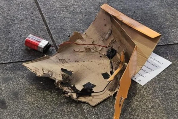 Imagem colorida mostra restos de caixa de papelão marrom queimados com uma pilha ao lado, jogados no chão