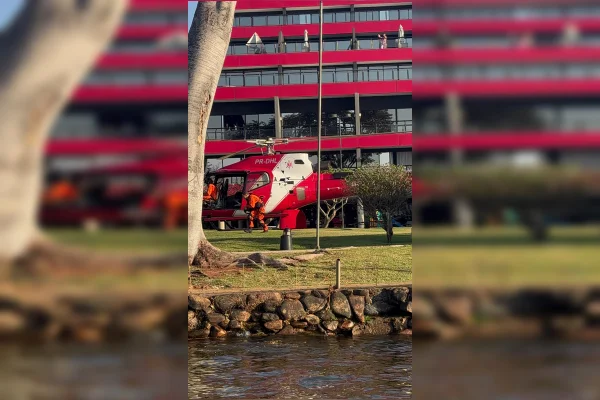 Imagem colorida de um helicóptero dos bombeiros pousado em um gramado em frente a um hotel