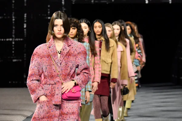 Fila de modelos mulheres e jovem no final do desfile da marca francesa Chanel. Ela usam roupas da marca. No fundo, é possível ver um painel de tecido quadriculado com a logo da marca. - Metrópoles
