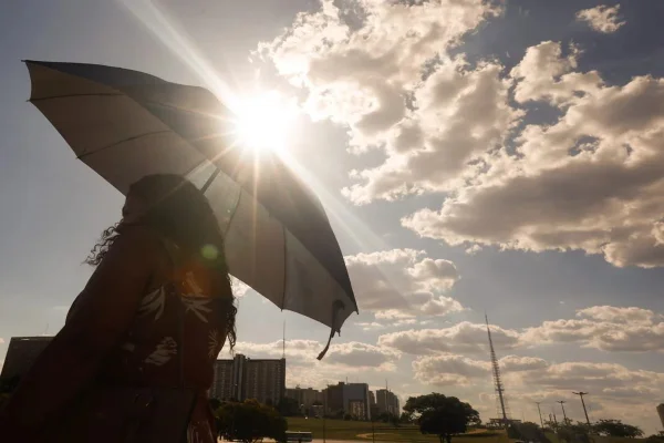 Imagem colorida mostra mulher segurando guarda-sol em dia de calor em São Paulo - Metrópoles