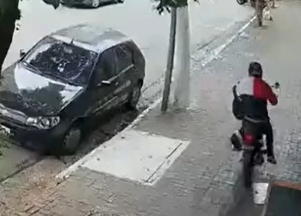 Imagem de câmera de segurança; um carro estacionado ao lado esquerdo e um homem, de costas, em cima de uma moto - Metrópoles