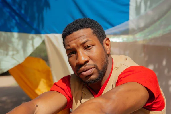 Jonathan Majors posa para foto de blusa creme com manga vermelha - Metrópoles