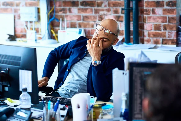 Homem cansado sentado à mesa em um escritório moderno. Metrópoles