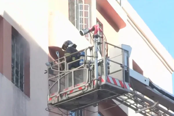 Imagem colorida de bombeiros em janela de prédio. Metrópoles