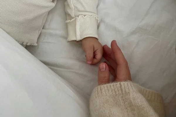 Mão de mãe encostando em mão de neném com cama no fundo - Metrópoles