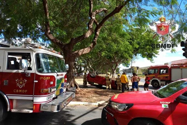 carro vermelho capotado ao fundo. à frente viaturas do Corpo de Bombeiros