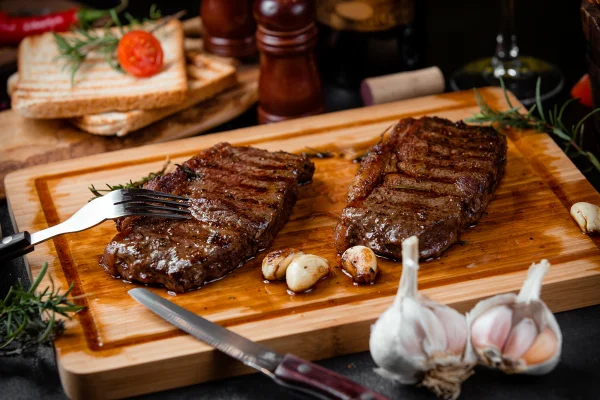 Pedaços de bife frito numa tábua de madeira e alhos. Metrópoles