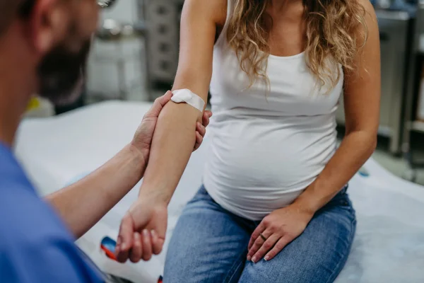 Ginecologista obstetra coletando amostra de sangue de gestante como parte do pré-natal. Gestante em consulta de acompanhamento gestacional no consultório médico. Metrópoles