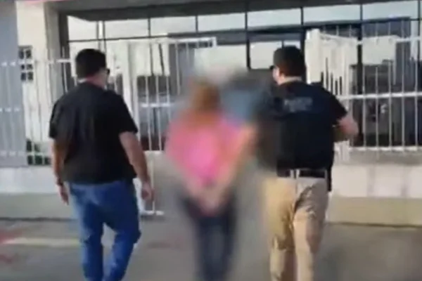 Imagem colorida de mulher presa sendo levada por policiais. Metrópoles