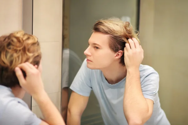 jovem se olhando no espelho e penteando o cabelo com as mãos. Avaliando a própria imagem - Metrópoles - dismorfia corporal