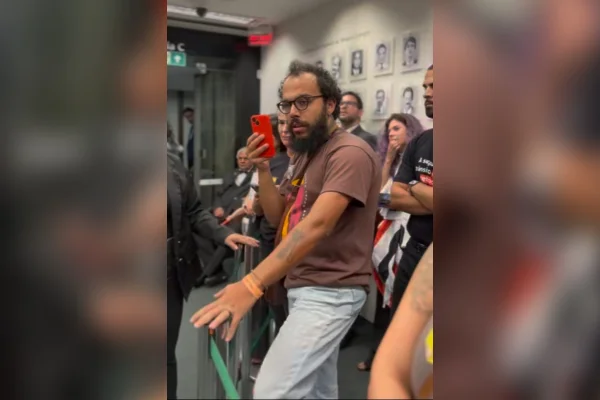 Homem de óculos com celular vermelho na mão - Metrópoles