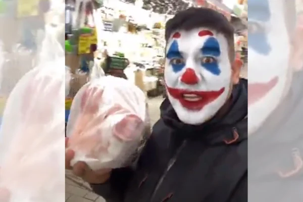 Imagem colorida de um torcedor com filtro de palhaço no rosto segurando uma cabeça de porco embalada em plástico - Metrópoles