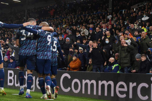 Na foto vemos três jogadores abraçados com uniformes azuis e ao fundo a torcida