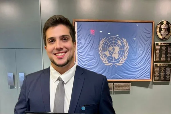 Secretário de Direitos Humanos de Niterói, Raphael Costa, em sala com títulos na parede. Ele é branco, cabelo curto e liso e sorri, usando terno - Metrópoles