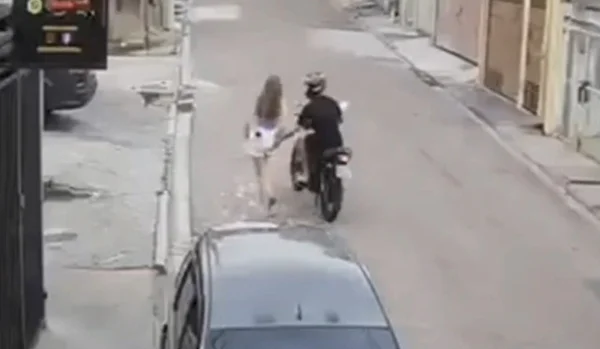 Imagem colorida mostra reprodução de câmera de segurança onde um homem vestido de preto em cima de uma moto passa a mão das nádegas de uma adolescente vestida de branco no meio da rua; motociclista foi preso - Metrópoles