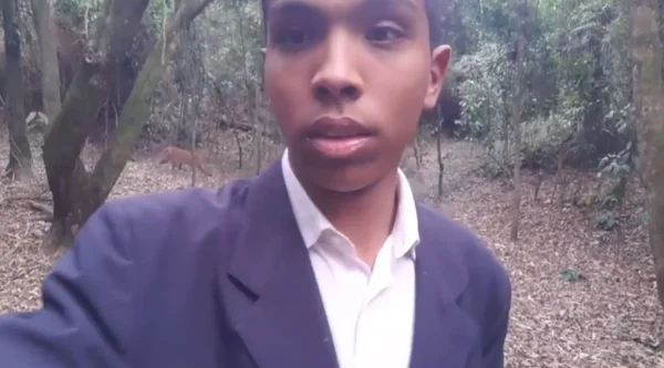 Imagem colorida mostra o pastor Paulo Henrique da Silva, um homem negro com um terno azul e uma camisa branca, em um parque cercado de árvores, e, ao fundo, uma onça-parda passeando - Metrópoles