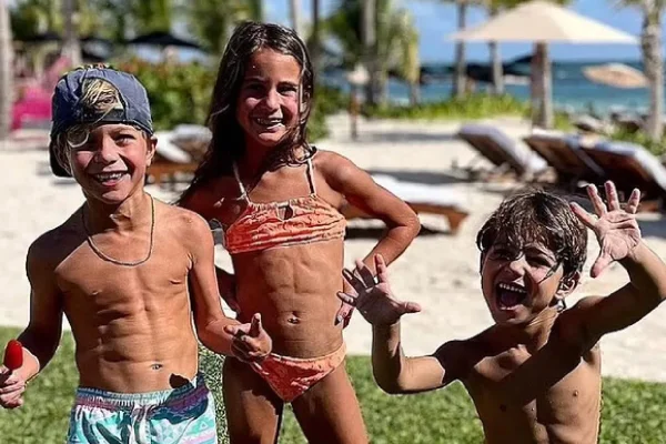 Foto colorida de 3 crianças, dois meninos e uma menina. Eles estão usando roupa de banho