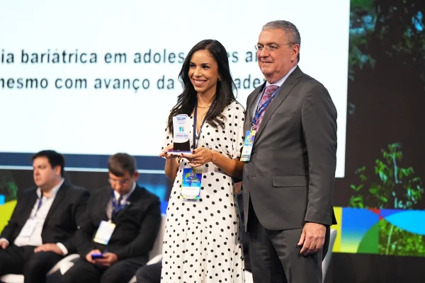 Foto de mulher de vestido branco segurando prêmio ao lado de homem de terno - Metrópoles
