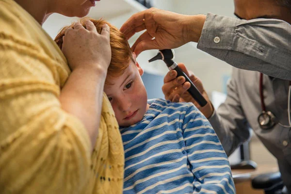 Médico examina orelha de criança enquanto mãe o abraça
