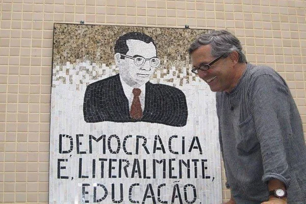 Foto colorida de Henrique Gougon em frente a mural feito por ele