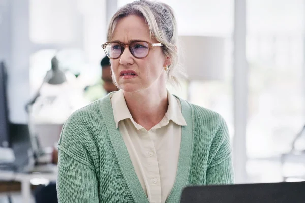 Funcionária, mulher e irritada no escritório irritada, frustrada e irritada no local de trabalho. Pessoa feminina, triste e chateada com colega em espaço de trabalho com cara de nojo, notebook e tecnologia para trabalhar - Metrópoles