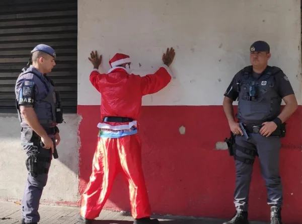 Imagem mostra Papai Noel, com mãos na parede, ao lado de PMs - Metrópoles