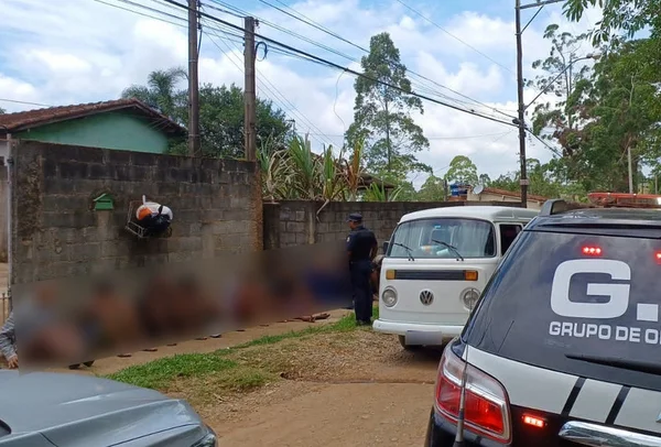 Imagem com pessoas sentadas em calçada, vigiadas por policial - Metrópoles