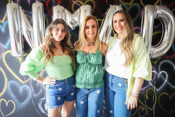Três mulheres em frente a balões e quadro desenhado