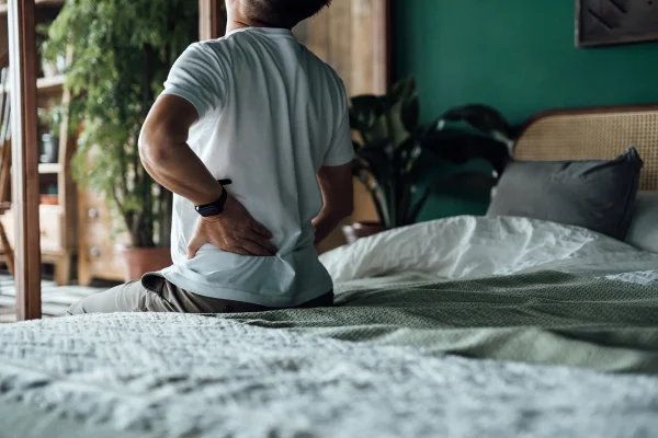 Imagem mostra homem sentado na beirada da cama com a mão nas costas, sentindo dor - Metrópoles