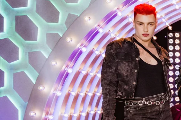 Foto colorida de Flavio Verne com cabelo vermelho e jaqueta preta com fundo colorido - Metrópoles