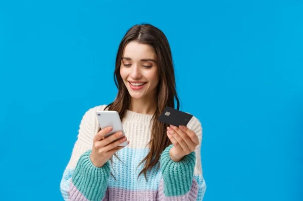 Mulher sorrindo com celular e cartão de credito