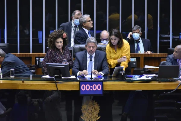 O presidente da Câmara dos Deputados, deputado Arthur Lira (PP-AL) fala ao microfone sentado em mesa diretora, cercado de assessores e deputados - Metrópoles