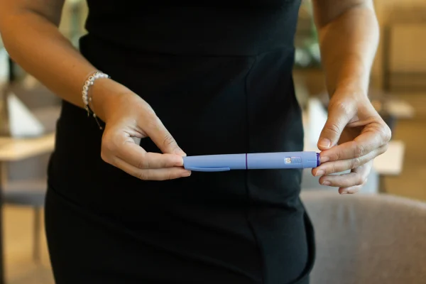 Foto de mulher com vestido preto segurando uma caneta a base de GLP-1 - Metrópoles.